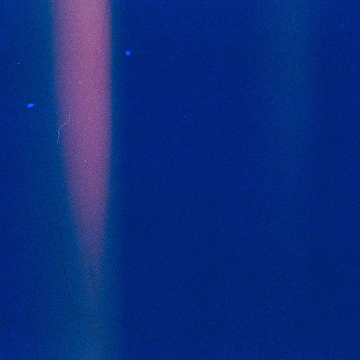 Billix website: Abstract film light leak: a soft pink beam of light across deep blue